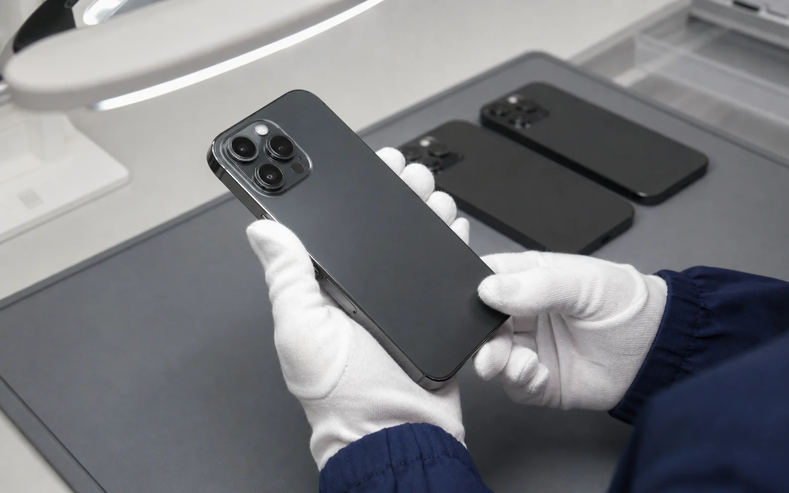 検品灯の下で中古スマートフォンの外観状態を確認するスタッフ